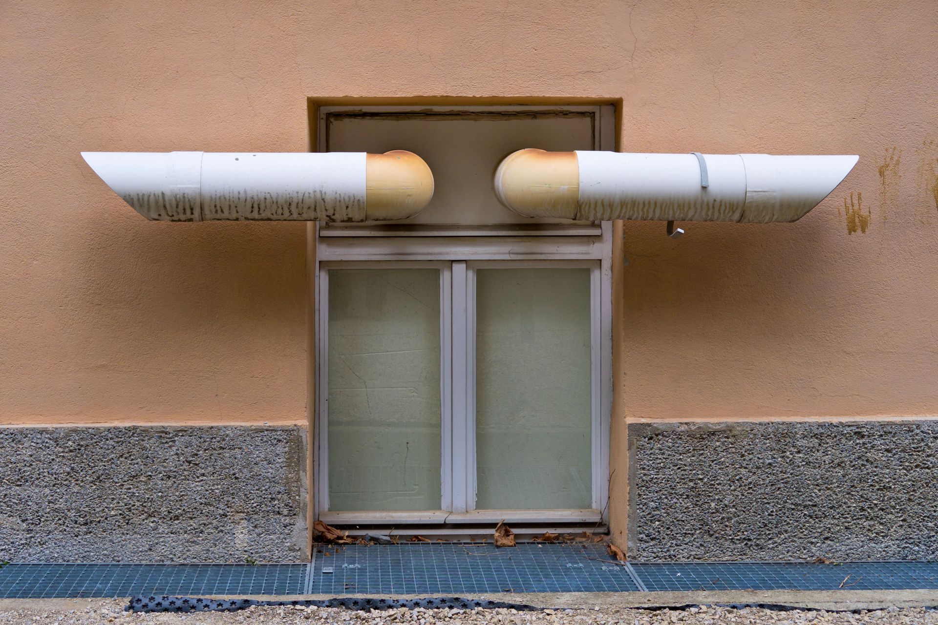 Close-up of industrial ventilation pipes above a window on a building wall.